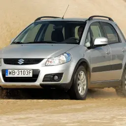 Srebrny Suzuki SX4 1.6 benzyna pokonuje piaszczystą wydmę, wzbijając tumany piasku.