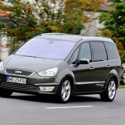 Brązowy Ford Galaxy MK2 w ruchu, z widocznymi felgami i tablicą rejestracyjną WE 2543U.