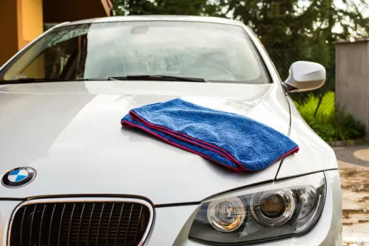 Niebieski ręcznik do osuszania auta leży na masce białego BMW. Idealny do rankingu najlepszych akcesoriów do pielęgnacji samochodu.