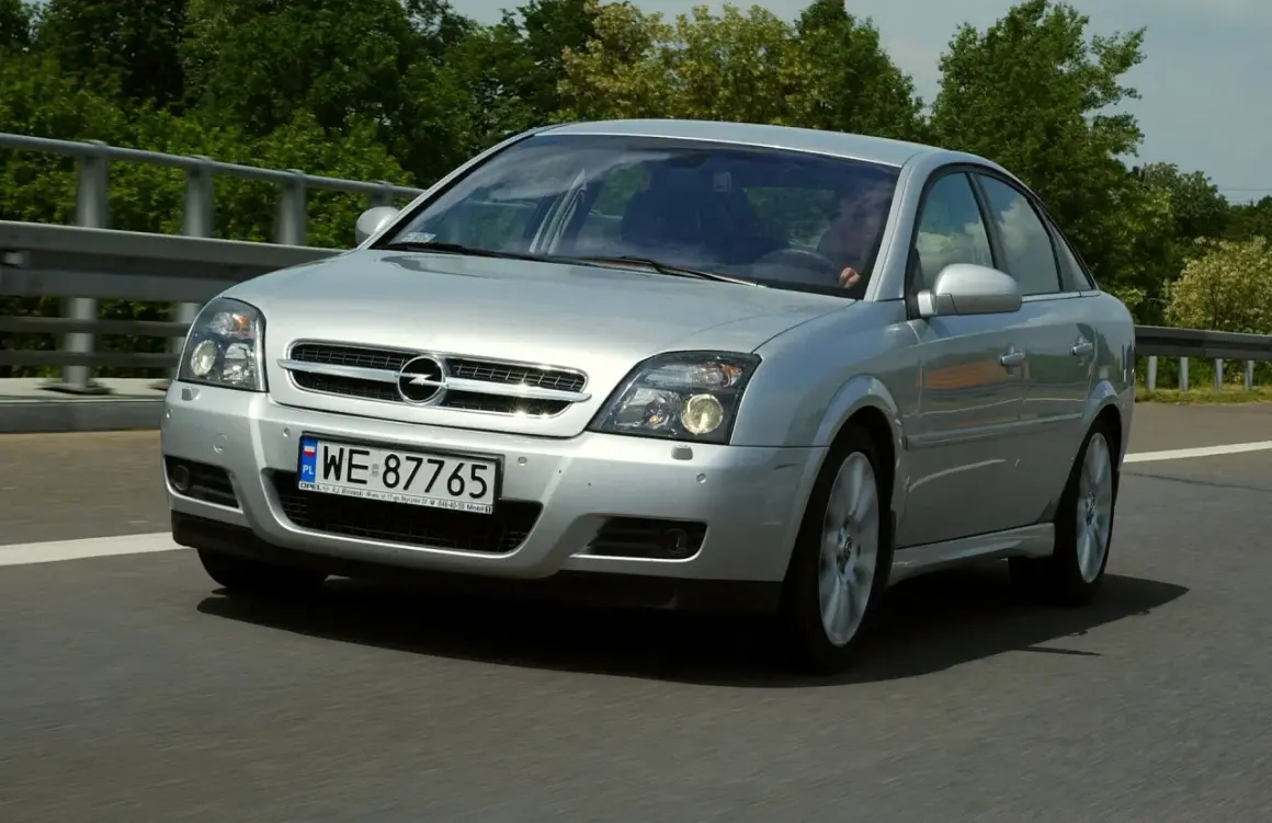 Srebrny Opel Vectra C 1.9 CDTI 150KM jedzie po drodze, otoczony zielenią.
