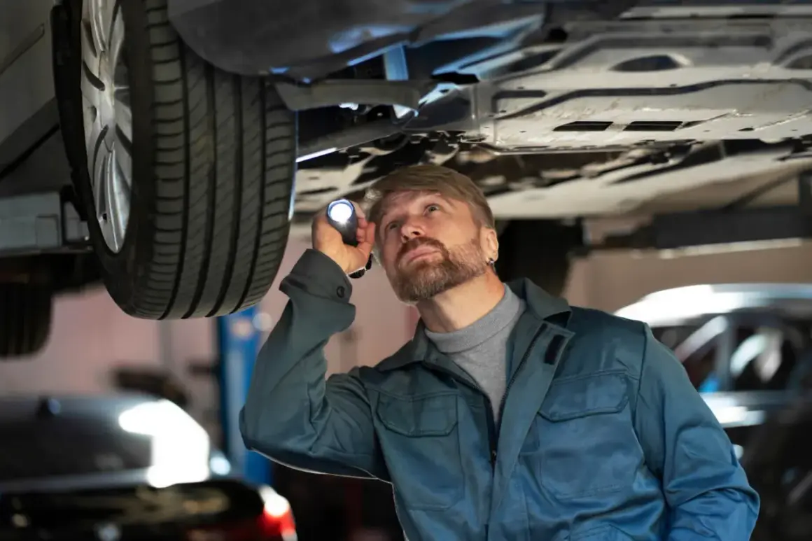 Mechanik z latarką bada podwozie auta, szukając usterki. Czy to jarzmo zawieszenia wymaga wymiany?
