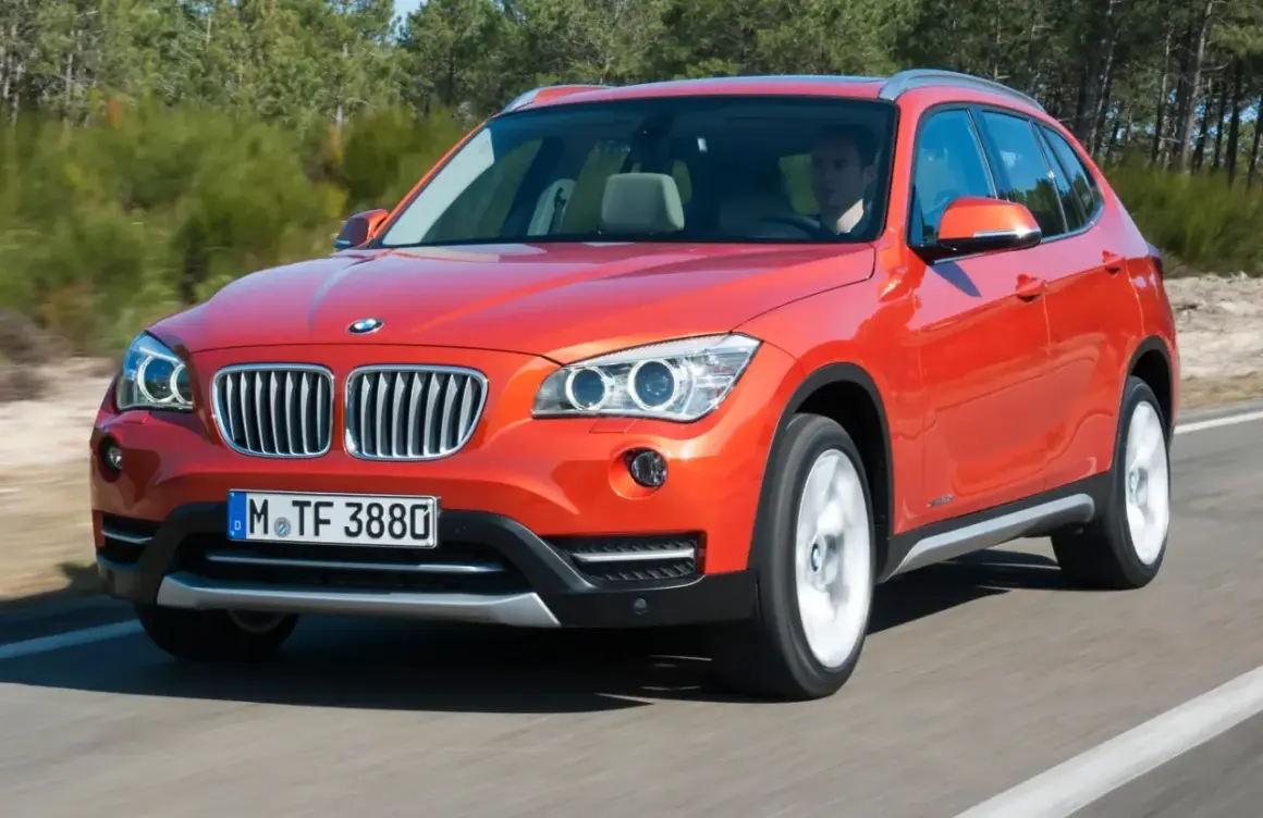 Pomarańczowy BMW E84 w ruchu, z widocznym kierowcą.