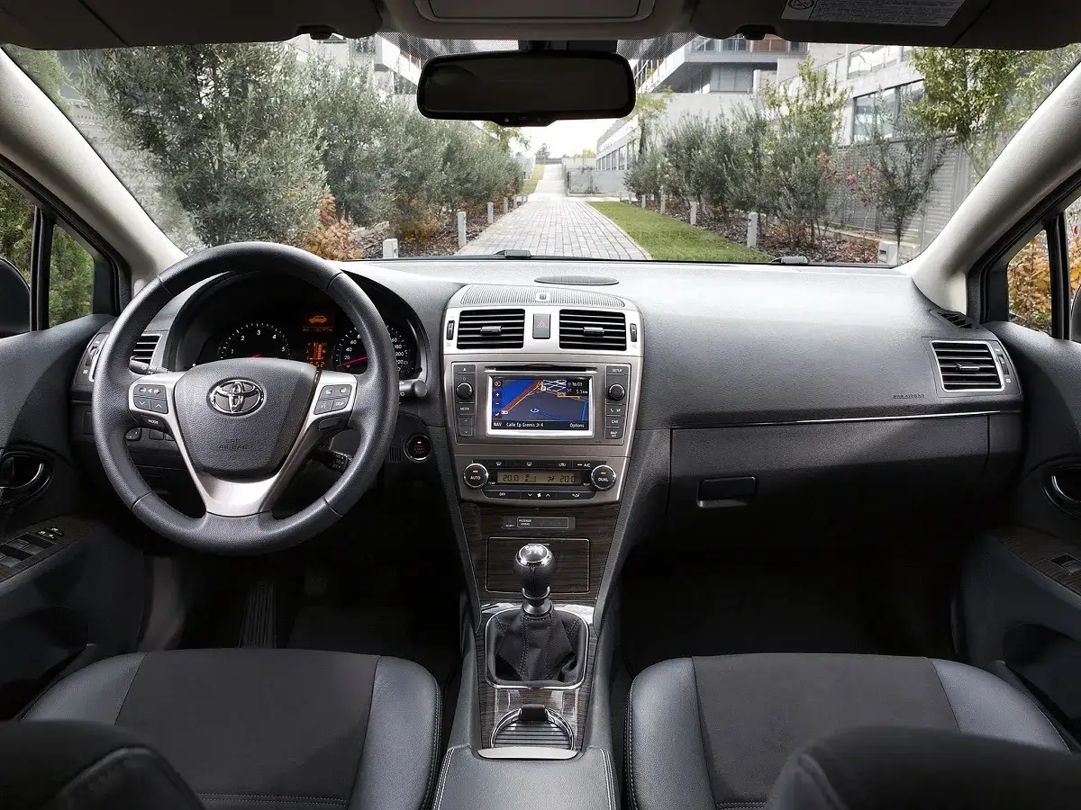 Wnętrze Toyota Avensis T27: kierownica, deska rozdzielcza z nawigacją, dźwignia zmiany biegów i fotele.