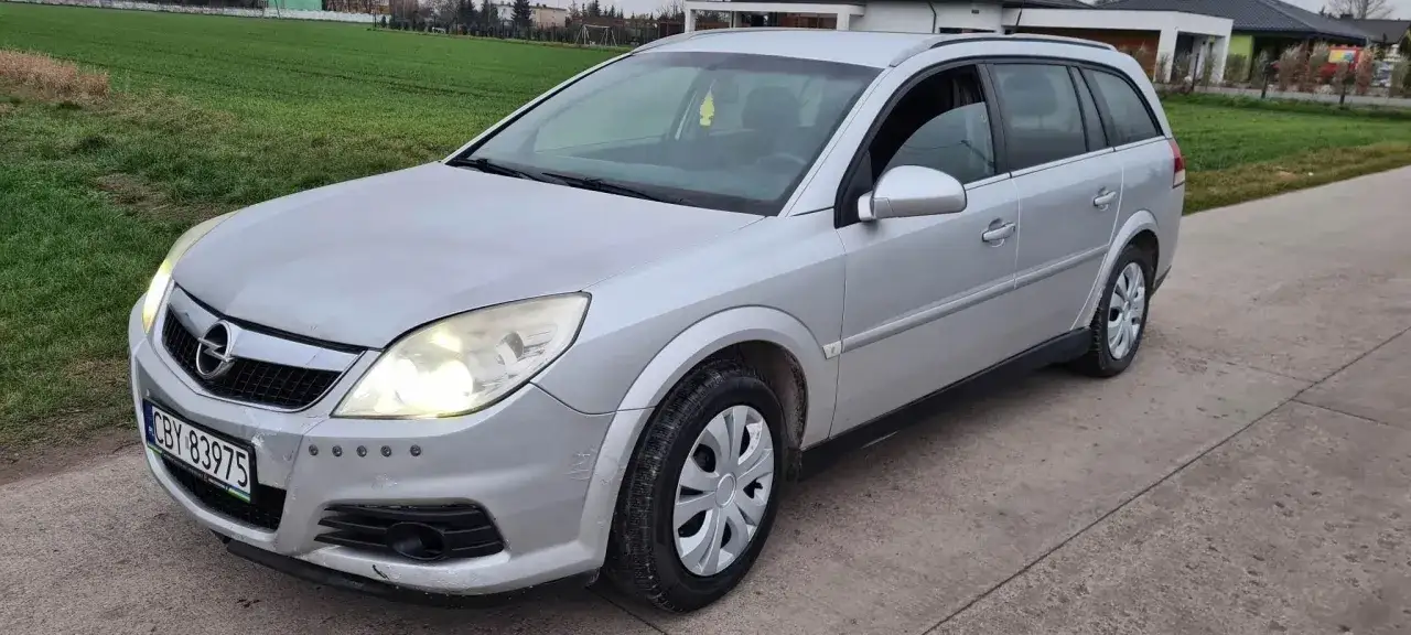 Srebrny Opel Vectra C 1.9 CDTI 150KM na tle zielonego pola i nowoczesnych domów.