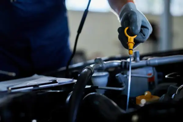 Mechanik w rękawiczce sprawdza poziom oleju za pomocą żółtej miarki. To ważny element kontroli silnika, podobnie jak sprawna odma olejowa.